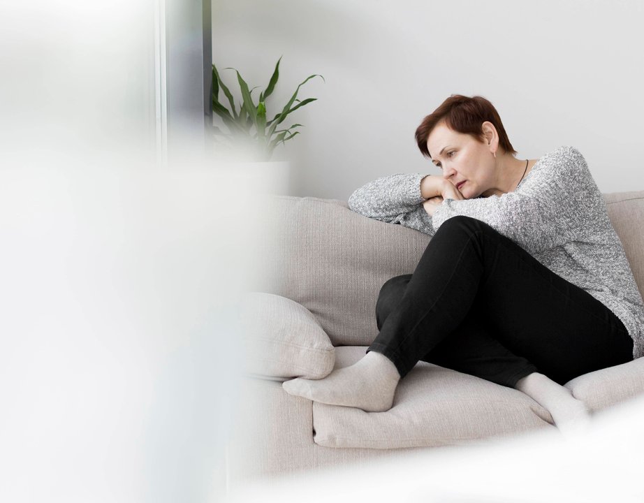 A woman sitting on a couch, arm laid on their shoulder, staring despondently into the distance.