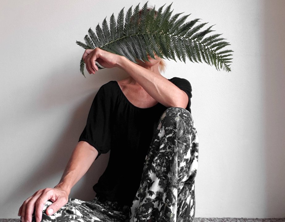 Woman holding a large fern leaf in front of her face.